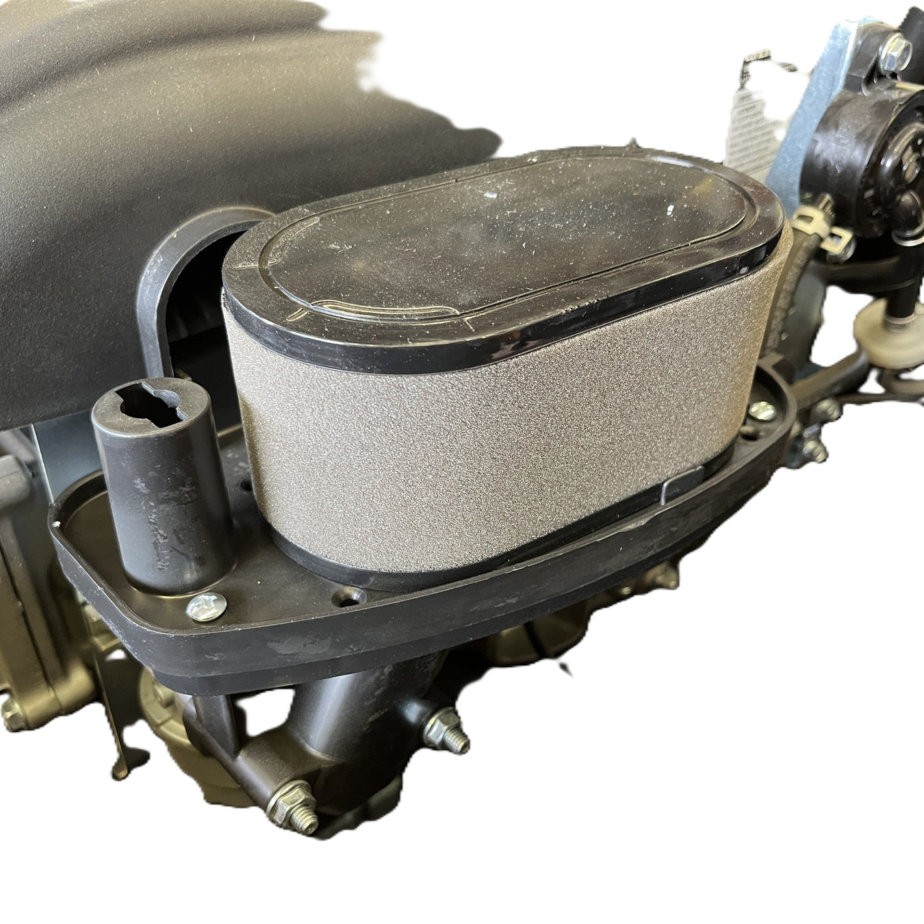Close-up view of a grey foam air filter attached to a motorcycle or small engine intake, with nearby metal and plastic components visible against a white background.