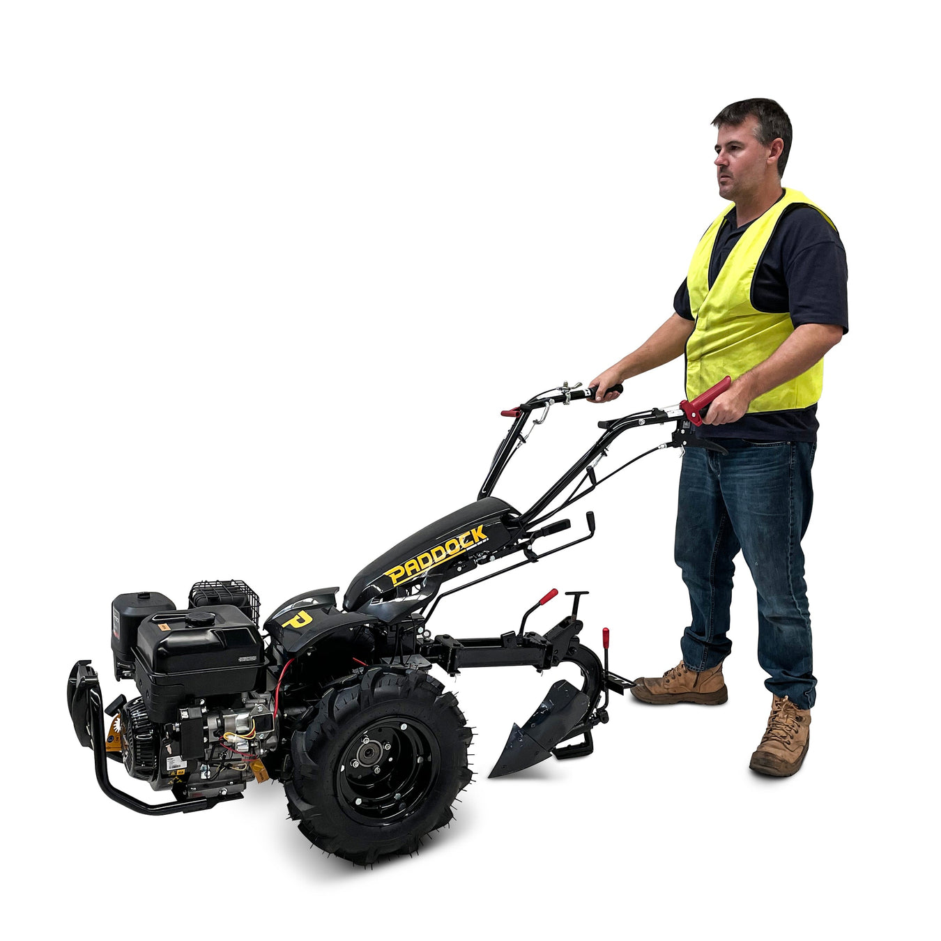 A man wearing a yellow safety vest and boots stands behind and operates a black Paddock rotary tiller machine against a plain white background.