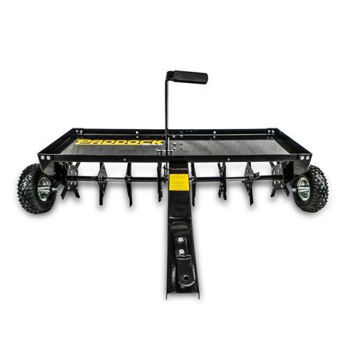 A black metal tow-behind dethatcher with spiked blades, two large wheels, and a central handle, designed for lawn and garden maintenance.