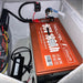 A large orange heavy-duty 36V Trolltek™ LiFePO4 Lithium Battery with Bluetooth, by Trolltek, is installed in a compartment with connected wires, a fuse, and a nearby battery charger. The setup features lithium batteries known for their long cycle life, all neatly organized inside a white enclosure.