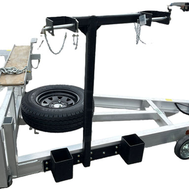 A close-up of the Paddock Excavator 2.9T Trailer Auger Rack & Well Mount shows metal beams, black brackets, chains, a mounted spare tire, and a wooden plank along the heavy duty machinery trailer frame.