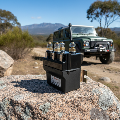 An Albright Winch Solenoid DC88P sits on a rock outdoors, with a green off-road SUV equipped with a Sherpa 4x4 winch parked nearby on a dirt road among trees and mountains under a clear blue sky.