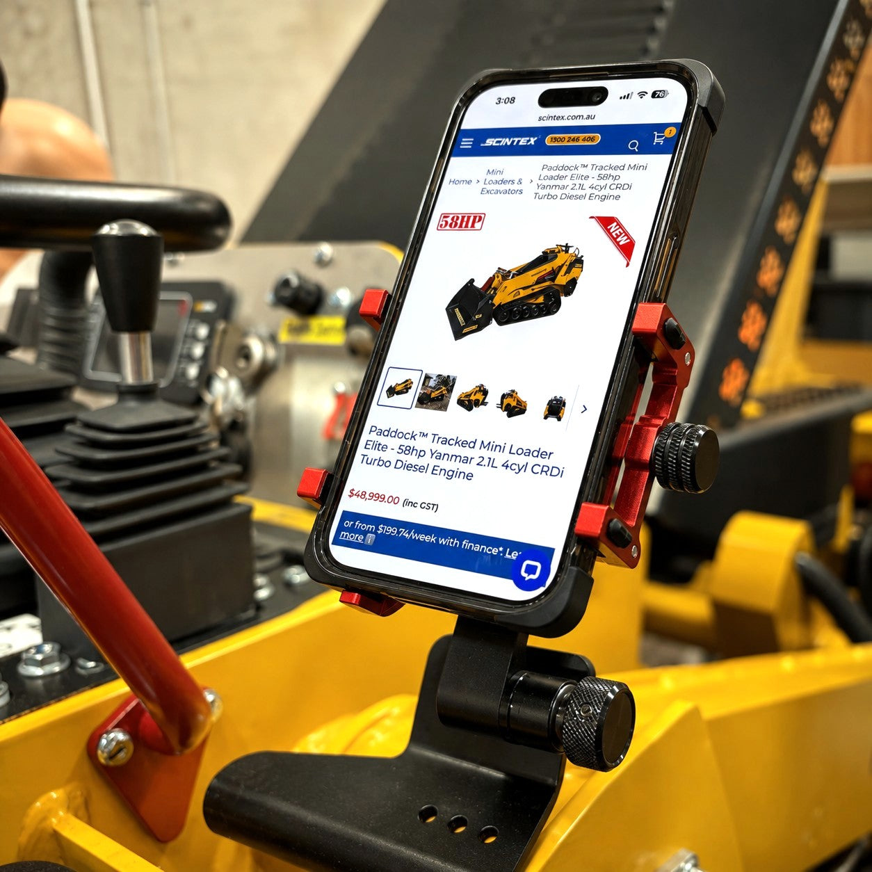 A smartphone, mounted inside construction equipment, displays a webpage featuring the Paddock™ Tracked Mini Loader Elite—a powerful 58hp Yanmar 2.1L 4-cylinder CRDi Turbo Diesel from Paddock—listed for sale. In the background, control levers and a blurred worker in safety gear emphasize the cutting-edge design and job site readiness of compact tracked loaders like this elite model for modern construction professionals.
