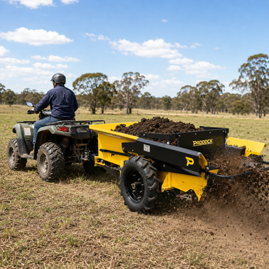 A person driving an ATV pulls a yellow Paddock Manure Spreader by Paddock, spreading soil or compost across a grassy field with trees and a blue sky in the background.