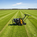A Paddock Turf Cutters - Self Propelled machine by Paddock, in yellow and black, is on a neatly striped lawn under a clear blue sky, surrounded by expansive green grass fields.
