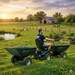 A man drives a Paddock RAT Ride-on Articulating Tipping Barrow beside raised garden beds on a farm at sunset, with chickens by a pond, donkeys, and a barn in the background.