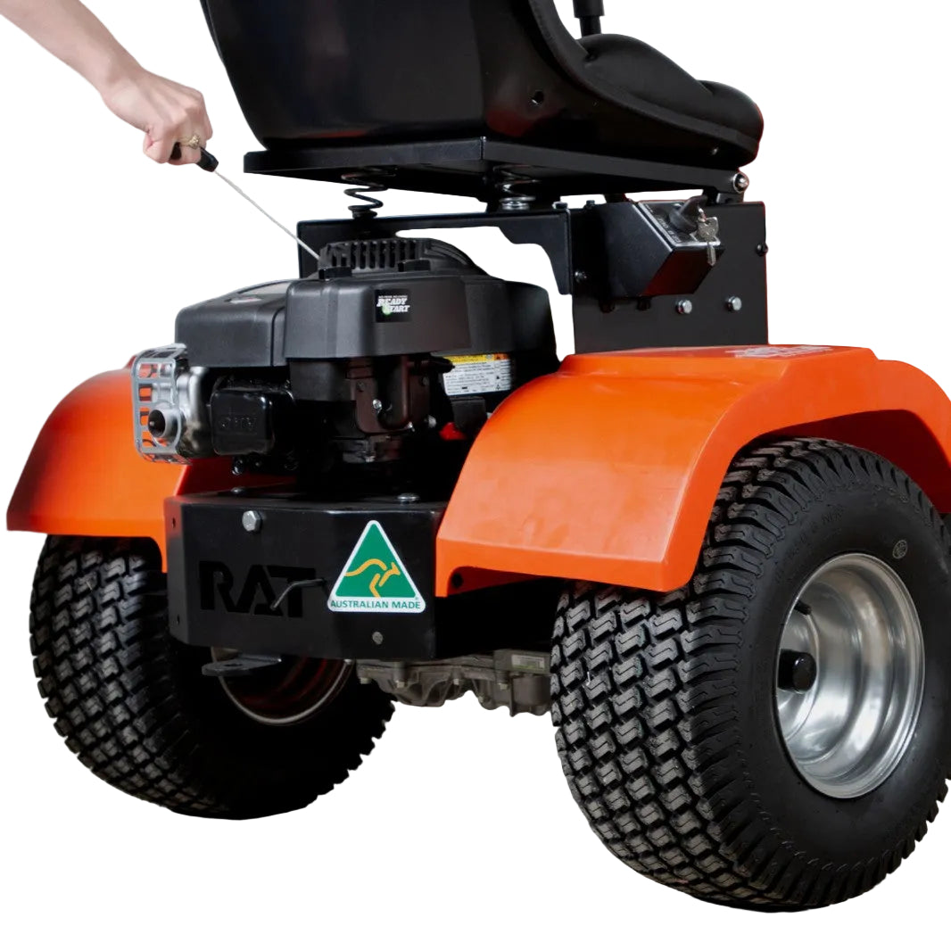 A person starts the engine of a Paddock RAT Ride-on Articulating Tipping Barrow, an orange mower with large black tires and an Australian Made sticker, featuring tipping barrow-inspired design.