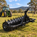 A Paddock™ 3-Point Drum Spike Aerator – 1500mm / 60″, Cat I by Paddock is positioned on grass in a sunny field with a green tractor and trees in the background, highlighting this effective tractor attachment designed to improve lawn health.