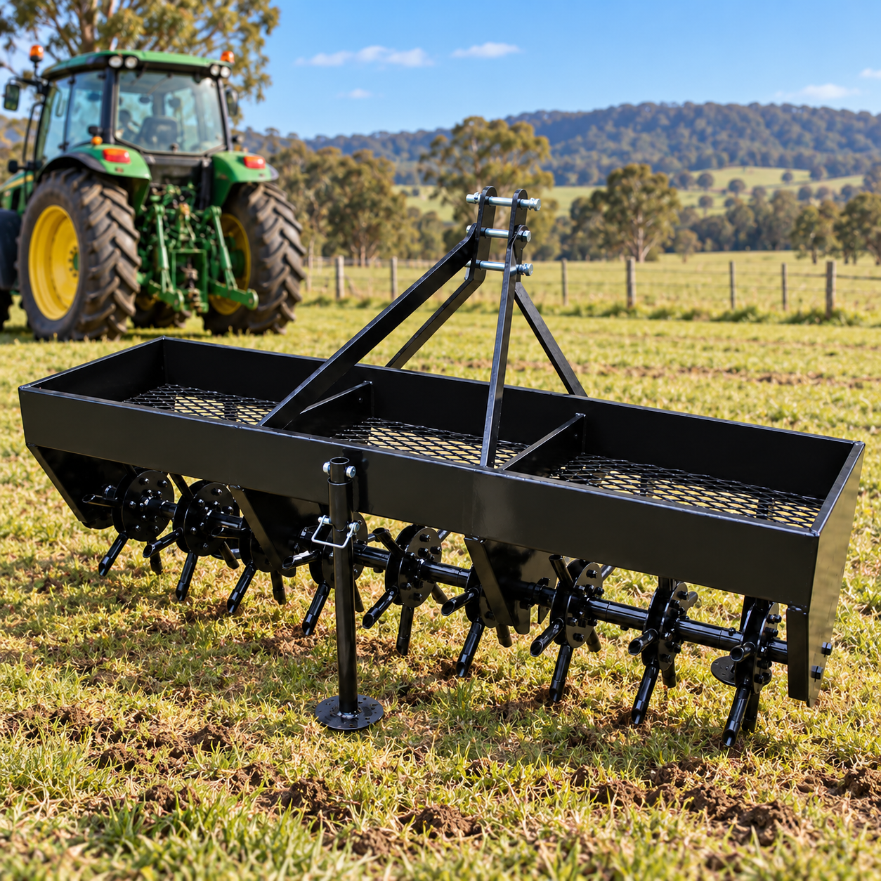 The Paddock™ 3-Point Plug Aerator – 60″ / 1500mm, Cat 0 & I by Paddock, a black core aeration tractor attachment, is positioned on grassy farmland with a green tractor slightly out of focus in the background and trees and hills visible in the distance.