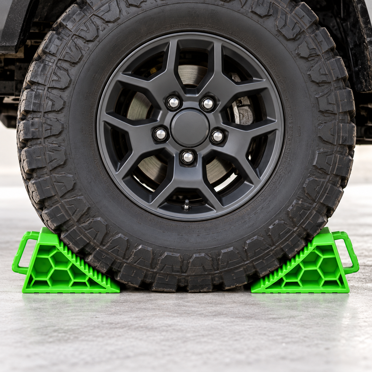 A large off-road vehicle tire secured by a Sherpa 4x4 Wheel Chock Set, featuring two bright green heavy-duty wheel chocks.