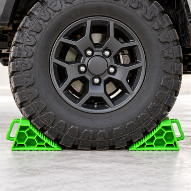 A large off-road vehicle tire secured by a Sherpa 4x4 Wheel Chock Set, featuring two bright green heavy-duty wheel chocks.