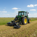 A green tractor with yellow wheels tows the Paddock PTO Rotary Mower with Swing Arm, cutting grass efficiently in a flat rural field under a blue sky. The Paddock brand ensures reliable mowing across expansive landscapes.