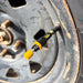 Close-up of a Sherpa 4x4 Tyre Deflators - 4pk unit attached to a vehicle’s valve stem, showing the yellow and black design and rusty metal wheel with lug nuts in the background.