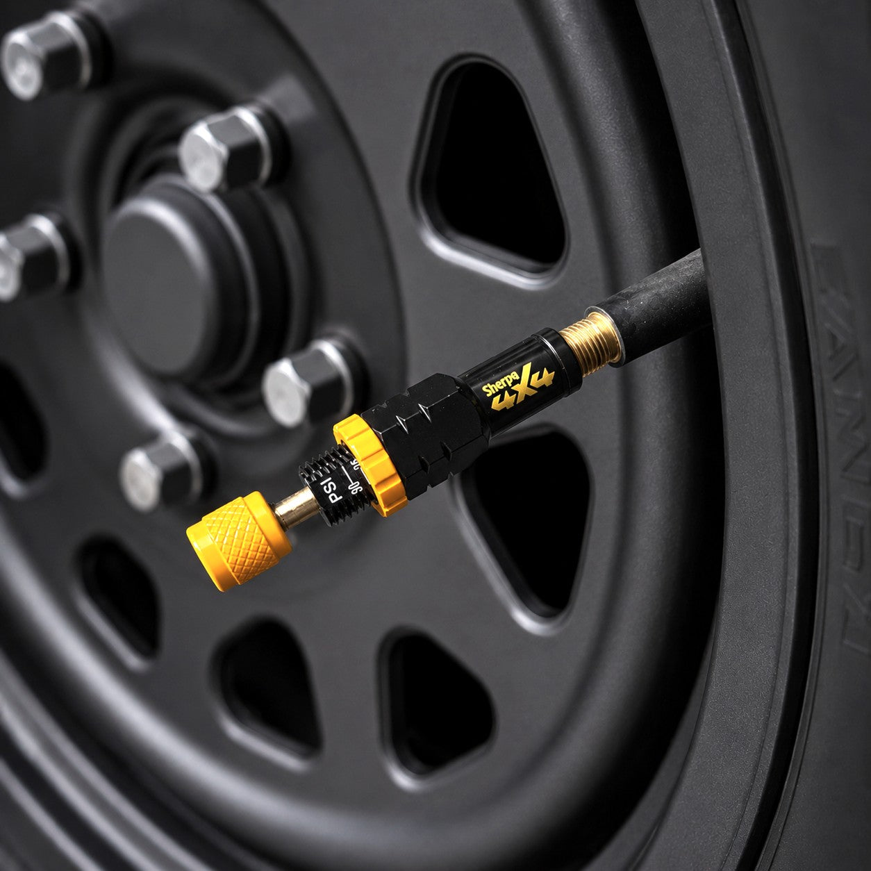 A Sherpa 4x4 Tyre Deflators - 4pk, in black and yellow, is attached to a car tire’s valve stem, with the tire and a rusty wheel rim from Sherpa 4x4 visible in the background.