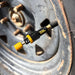 A Sherpa 4x4 Tyre Deflators - 4pk, in black and yellow, is attached to a car tire’s valve stem, with the tire and a rusty wheel rim from Sherpa 4x4 visible in the background.