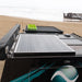 A close-up of Enerdrive Fixed Mono Solar Panels with a black frame mounted on a vehicle parked on a sandy beach, set against the ocean and a rusted shipwreck.