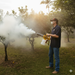 A person uses the Paddock Portable Thermal Insect Fogger by Paddock to spray pesticide on fruit trees in an orchard during daylight for effective pest control.