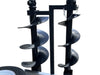 Two large black auger drill bits are mounted vertically on a metal frame from the Paddock Mini Loader & Excavator Alloy Equipment Trailers by Paddock. Part of a custom alloy trailer and a white tire are visible at the bottom left against a white background.