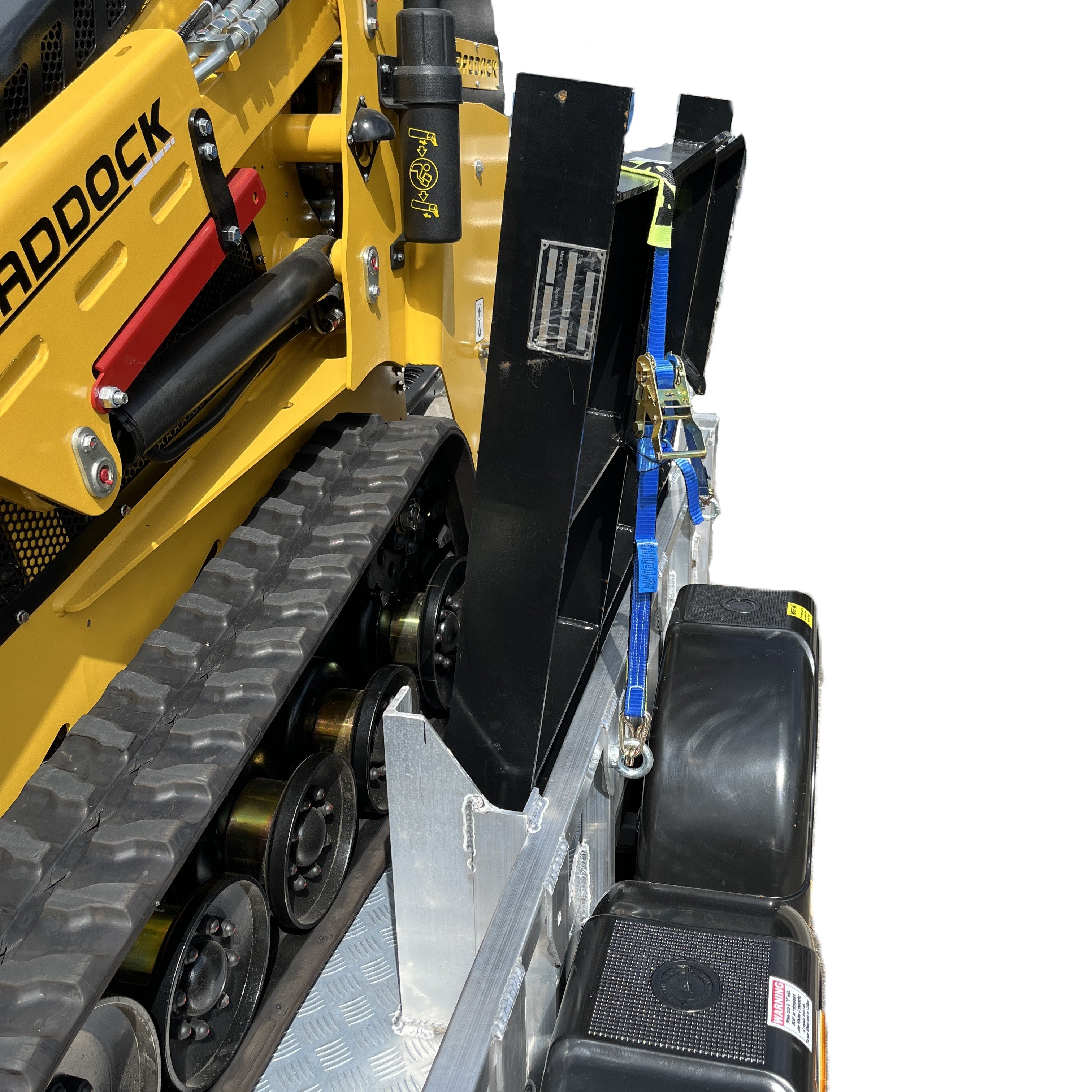 Close-up of a yellow tracked vehicle on a Paddock Mini Loader Trailer Spreader Bar Mount, secured with blue straps. The silver diamond-plate trailer highlights the quality of Australian made Paddock equipment. Background is white.