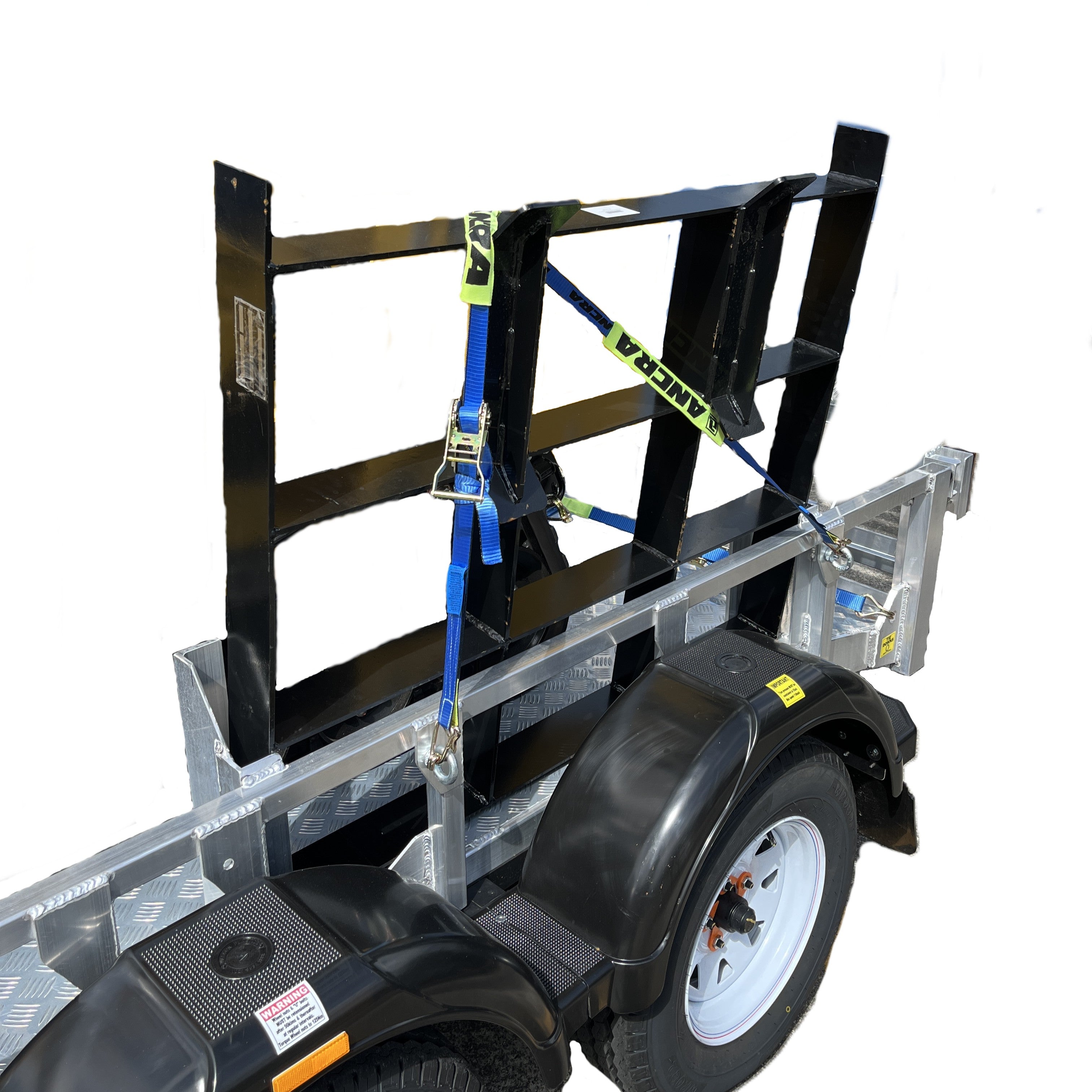 A Paddock Mini Loader & Excavator Alloy Equipment Trailer by Paddock, Spreader bar with black metal supports, blue and yellow straps, diamond plate flooring, and a white wheel, is parked on concrete near a blue wall.