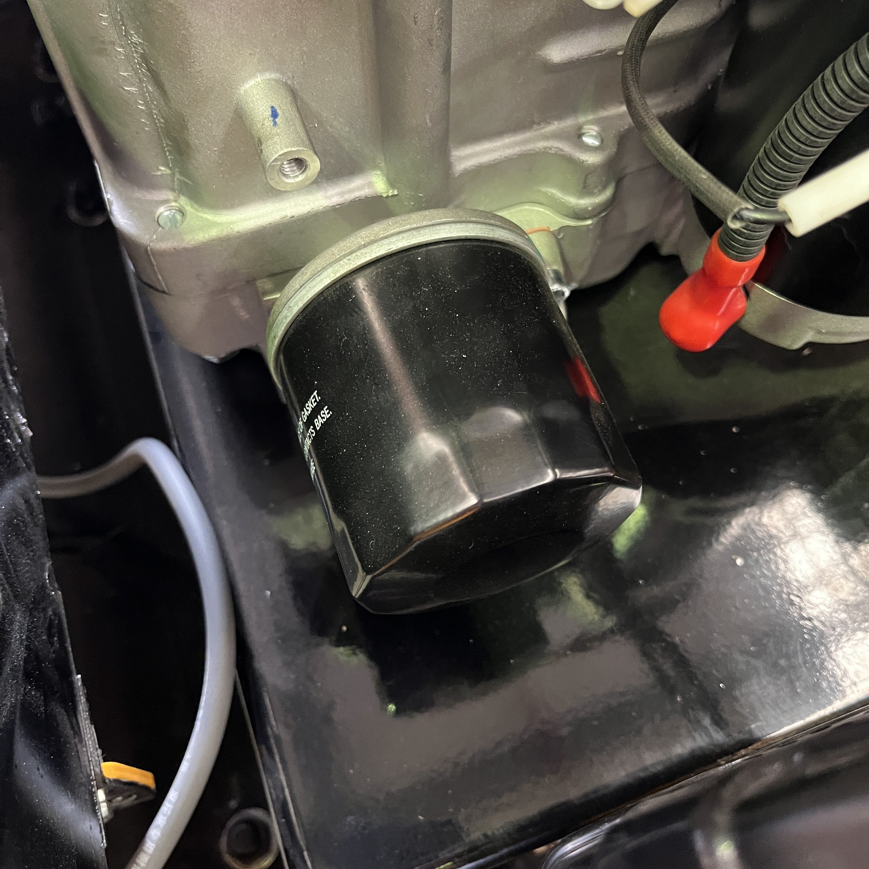 Close-up of a Paddock Loncin Oil Filter attached to a metallic engine block, with wires and cables on a glossy black surface—perfect for maintaining your RC Mower.