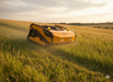 A Paddock Remote Controlled Mower 16HP with 1100mm twin blade design and track drive cuts tall grass on a gently sloping field under a partly cloudy sunset sky.