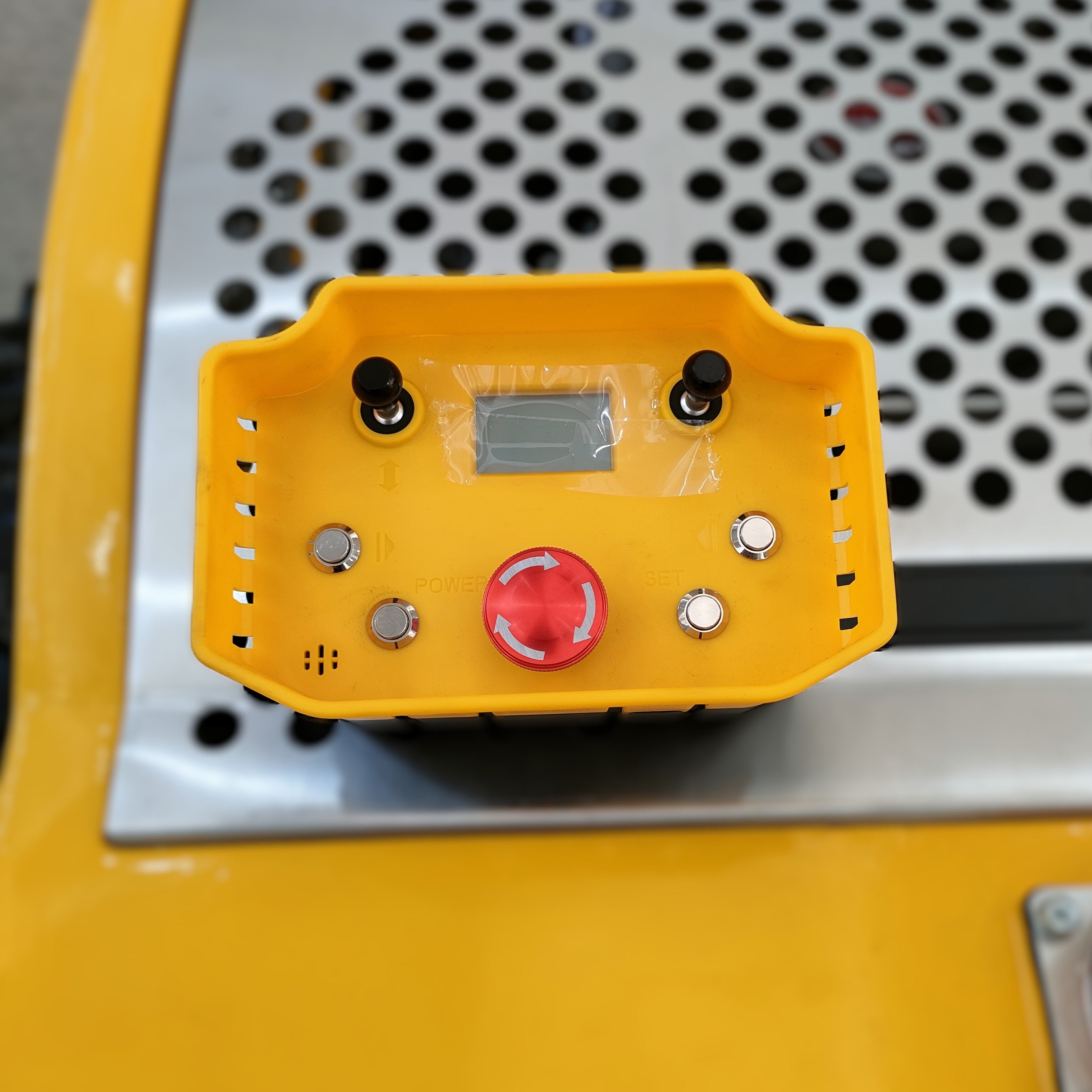 The Paddock Remote Controlled Mower 7.5HP - 530mm features a yellow industrial control panel with a large red emergency stop, display screen, four metal buttons, two black switches, and ventilation holes on a perforated metal surface.