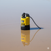 The Paddock Puddle Sucker Pump by Paddock features a yellow body with a black base and cable, standing in muddy water and reflecting on the surface—perfect for applications needing an efficient puddle pump.