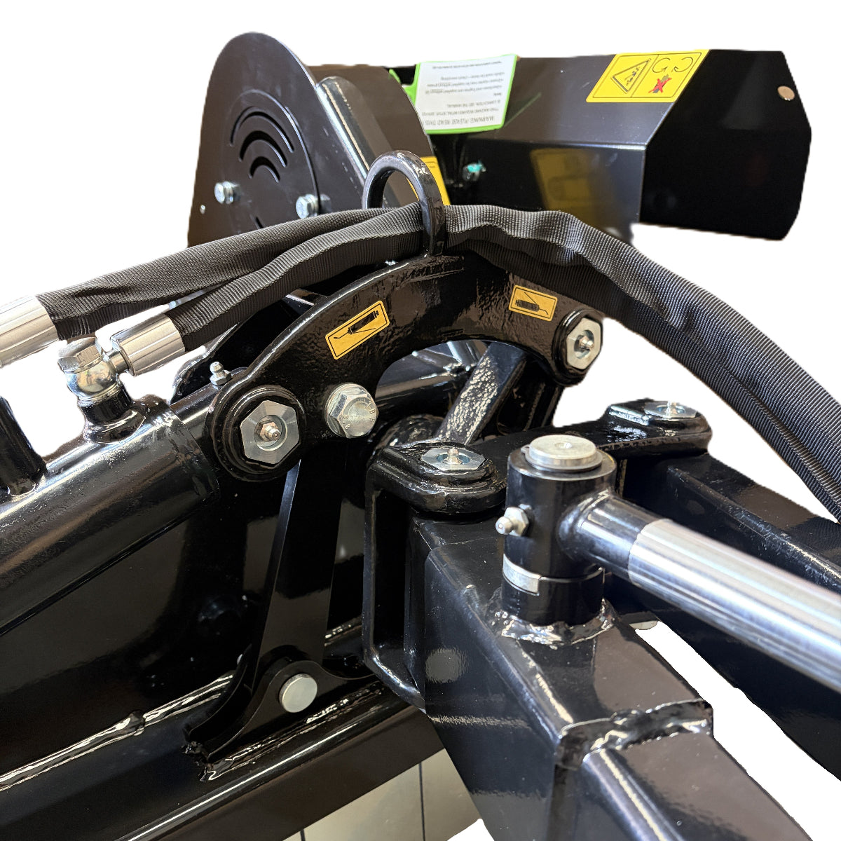 Close-up of metal components and fittings—including bolts, hydraulic hoses, and warning labels—on the Paddock™ PTO Offset Verge Flail Mower by Paddock. The parts are finished in black with yellow highlights, set against a white background.