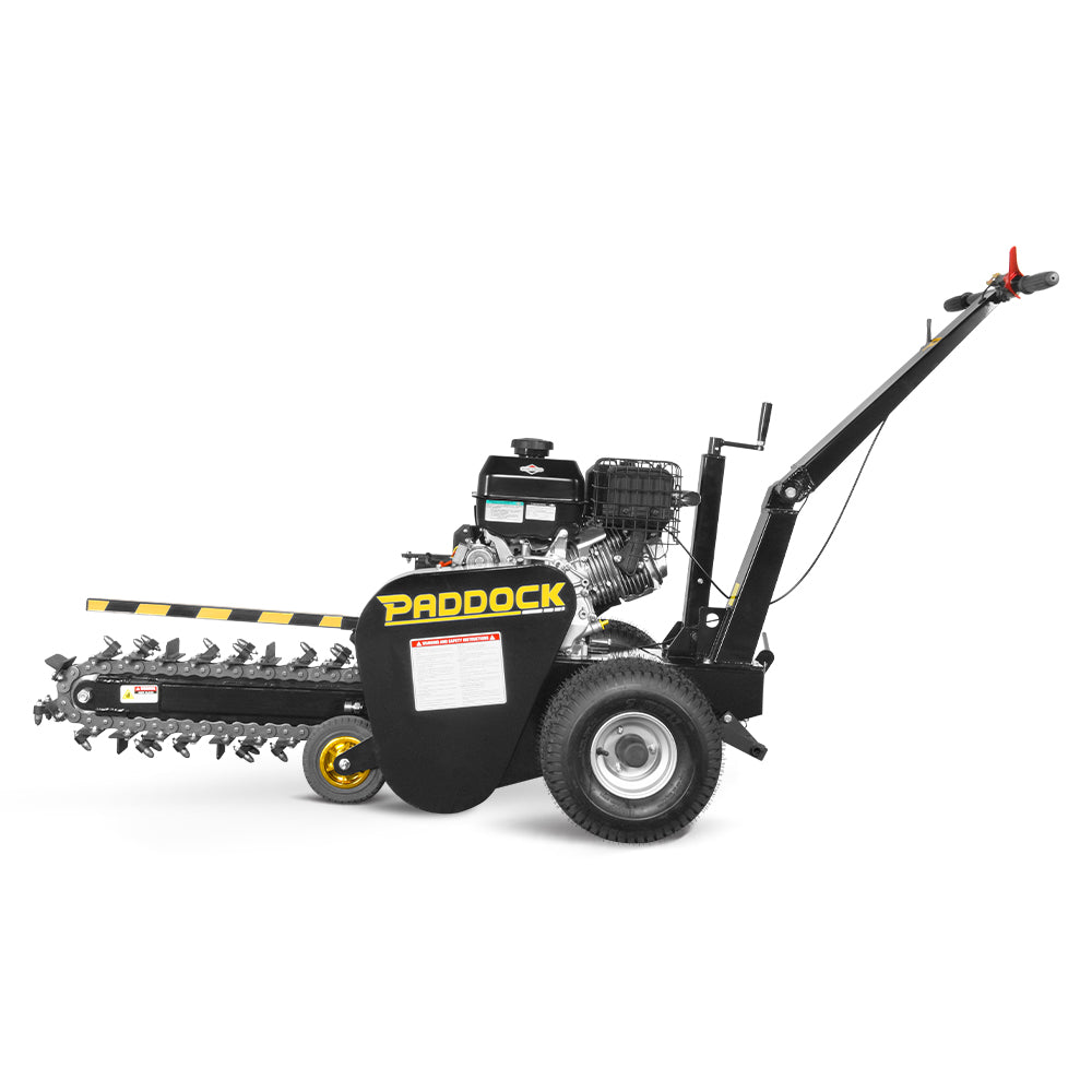 Side view of the Paddock Walk Behind Trencher with Guide Wheel, featuring a long rotating blade, two large wheels, handlebar for manual operation, black and yellow Paddock branding, safety labels, and a reliable Briggs & Stratton engine.