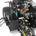 Close-up of the Paddock Walk Behind Trencher with Guide Wheel by Paddock, showing exposed engine components, wires, warning labels, large tires, and part of the toothed rotating mechanism.