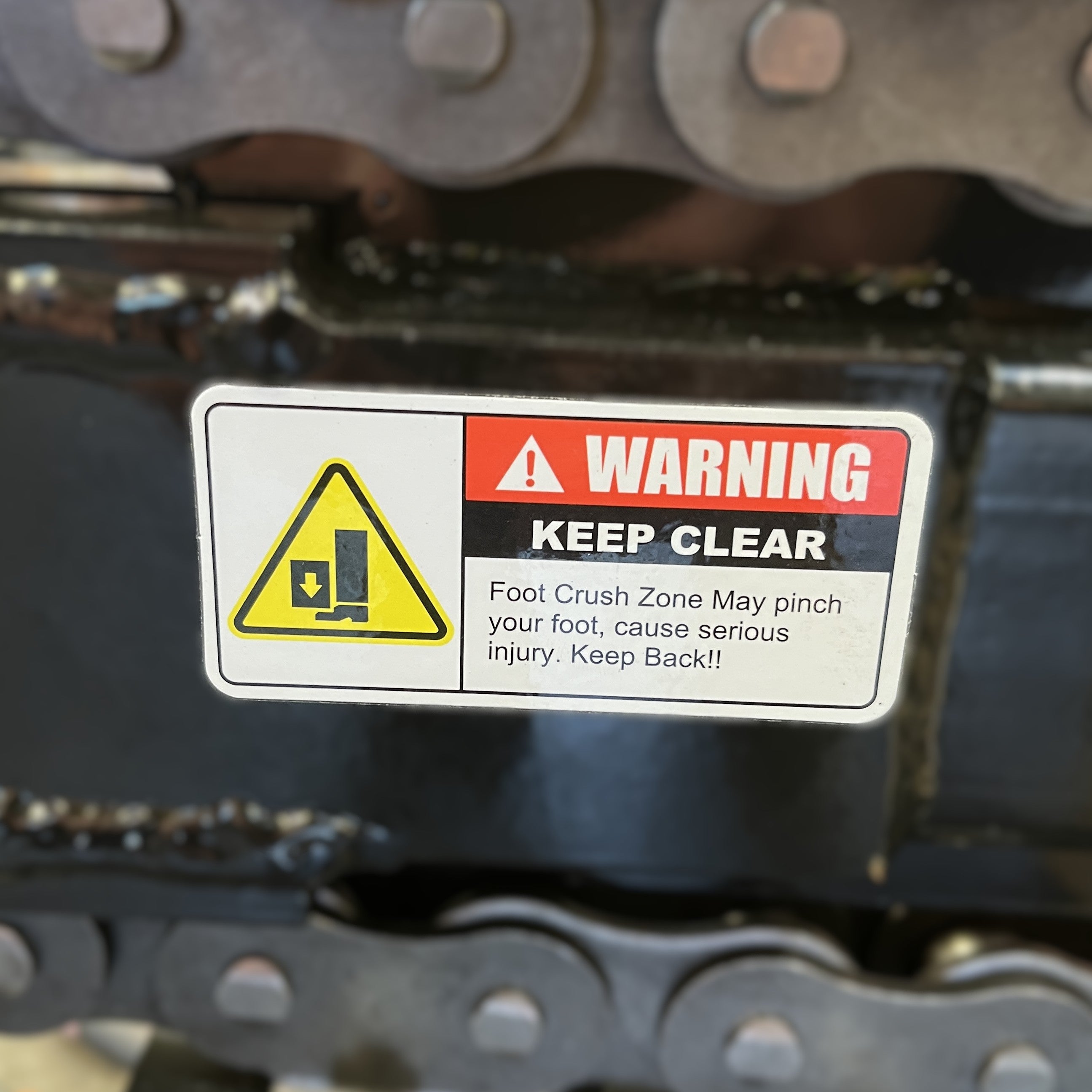 WARNING KEEP CLEAR. Foot Crush Zone on Paddock Walk Behind Trencher with Guide Wheel may pinch your foot, causing serious injury. Keep Back! Yellow symbol shows a foot being pinched. For use with Paddock portable trencher models.