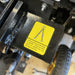 A yellow warning label with a chain symbol on the Paddock Walk Behind Trencher with Guide Wheel warns: Lifting points are marked by decals; lifting elsewhere is unsafe and may damage the machine. A tire is visible in the background.