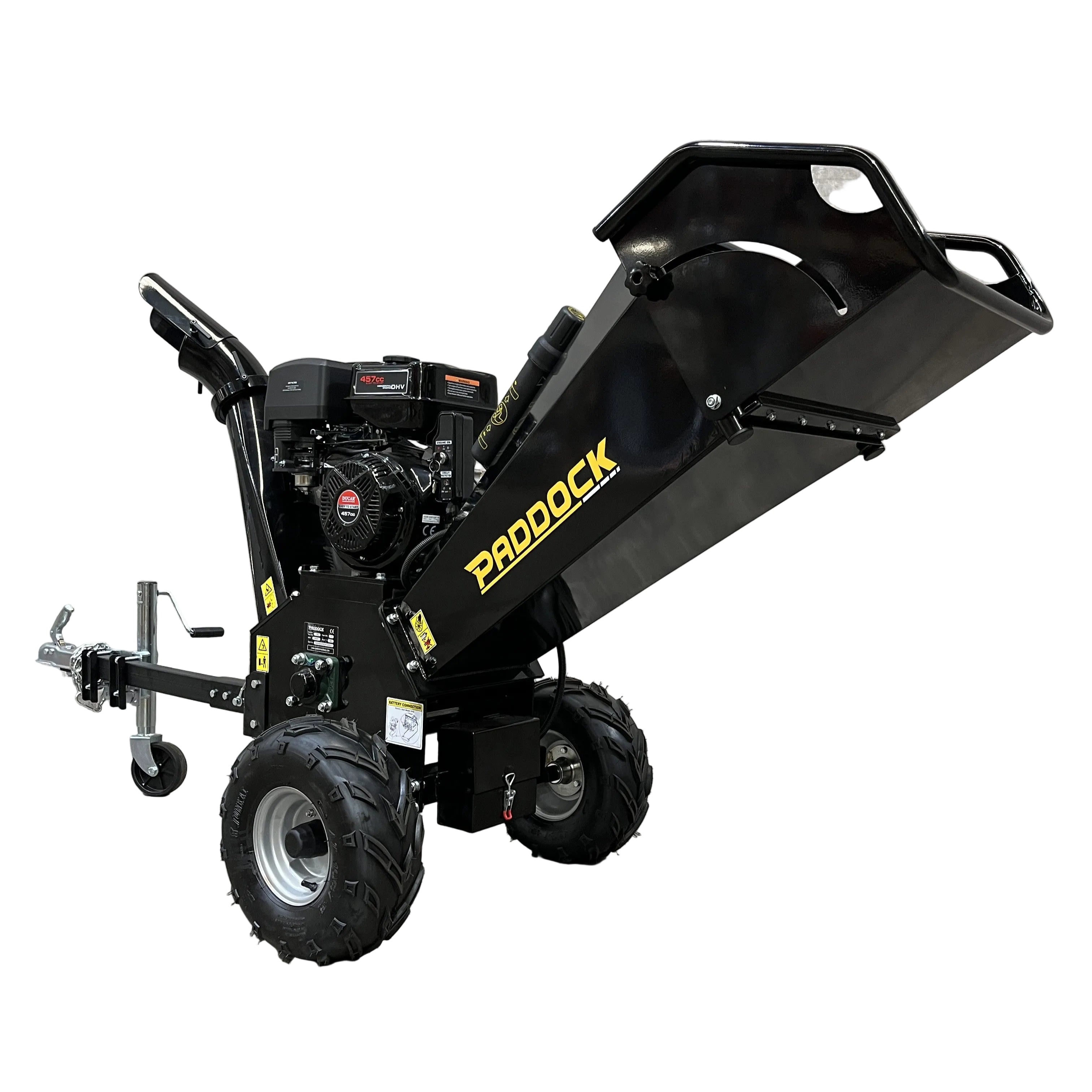 A heavy-duty black motorised wheelbarrow is parked indoors on concrete with its metal hopper tilted up, while a Paddock Wood Chipper Mulcher stands nearby, both highlighting this versatile workspace against the plain wall.