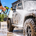 A person using a Paddock™ Pressure Washer Snow Foam Cannon – 1L, 4000 PSI to spray thick cleaning foam onto a muddy off-road vehicle.