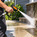 A person uses the Paddock™ 5000 PSI Brass Jetting Trigger Gun by Paddock to clean dirty concrete steps outside, powerfully spraying water to remove grime and debris. Greenery is visible in the background as this robust brass trigger gun ensures a thorough clean.