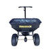 Front view of the Paddock Fertiliser & Seed Spreader, a black heavy-duty walk-behind unit with a handle, clear plastic cover, large rugged tires, and bold yellow Paddock branding, ideal for lawns, isolated on a white background.