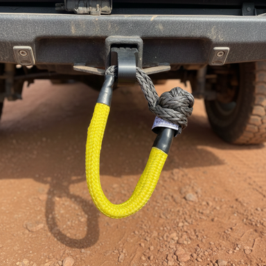 The Sherpa 4x4 Recovery Hitch & Soft Shackle Bundle from Sherpa 4x4 is shown attached to a vehicle’s rear, featuring a bright yellow synthetic rope shackle against reddish dirt—an essential, rugged recovery accessory for 4x4 adventures.
