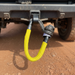 The Sherpa 4x4 Recovery Hitch & Soft Shackle Bundle from Sherpa 4x4 is shown attached to a vehicle’s rear, featuring a bright yellow synthetic rope shackle against reddish dirt—an essential, rugged recovery accessory for 4x4 adventures.