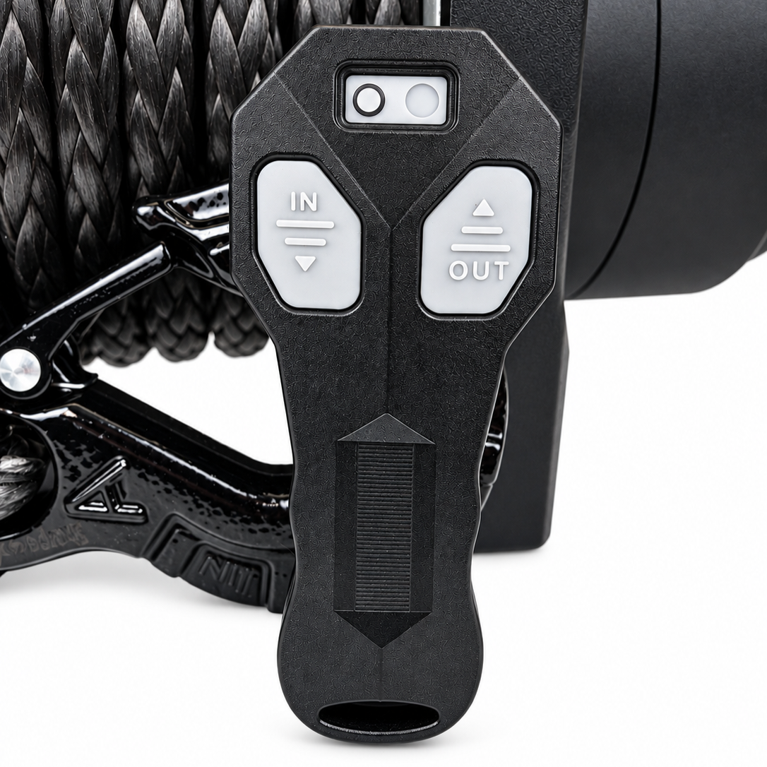 Close-up of a black remote control with IN and OUT buttons, displayed against the coiled synthetic rope of the Sherpa 4x4 Black Edition ‘Stallion’ 25,000Lb Winch—perfect for demanding heavy recovery situations.