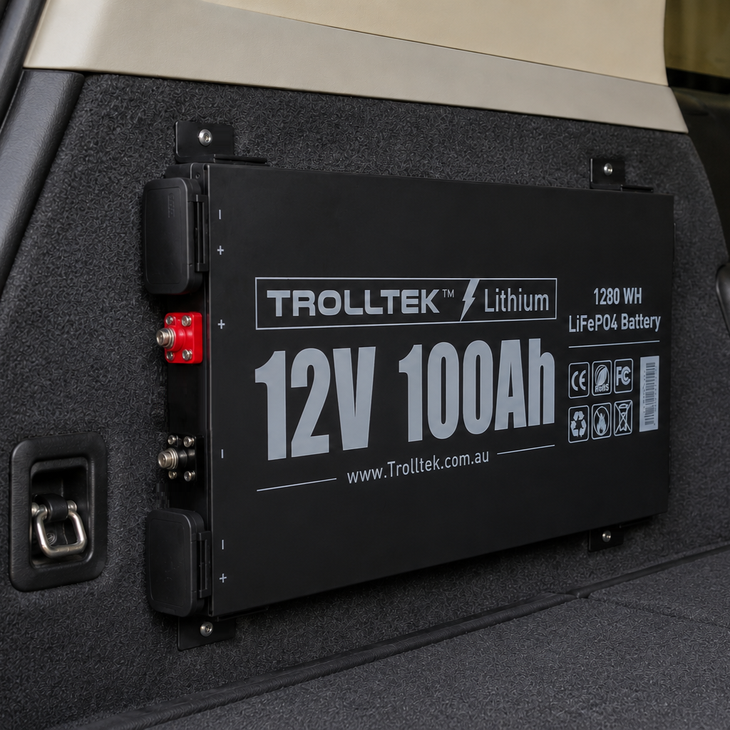 A Trolltek™ 12V LiFePO4 Lithium Slimline Battery 4WD Bundle – Charge While Driving (DC) is mounted on the interior wall of a vehicle, with visible cables and connectors on the side. This black battery setup from Trolltek is designed for easy integration with a DC/DC charger featuring an MPPT solar regulator, providing optimal off-grid power management for 4WD applications.