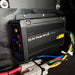 A Trolltek™ 40Amp DC/DC Charger with MPPT Solar Input by Trolltek in black is mounted on a wall. Colorful cables—blue, red, yellow, green, and black—connect at the bottom of the device. A prominent yellow caution sticker is visible. Designed as a reliable DC to DC Lithium Battery Charger for versatile applications, it also serves efficiently as an MPPT Solar Regulator for optimal performance.