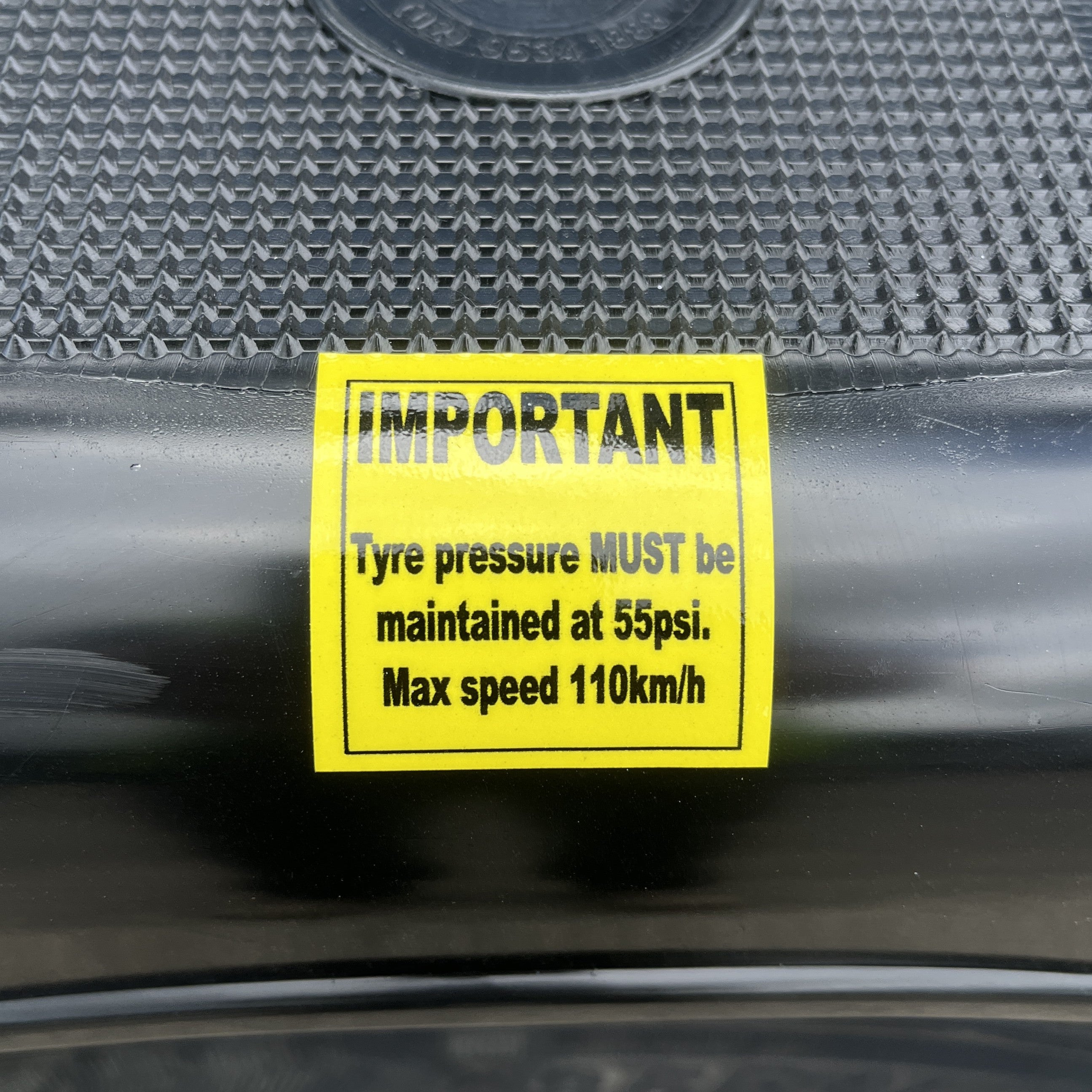 A yellow "IMPORTANT" label states: Maintain tyre pressure at 55psi, max speed 110km/h, on a black textured surface—perfect for Paddock Mini Loader & Excavator Alloy Equipment Trailers by Paddock.