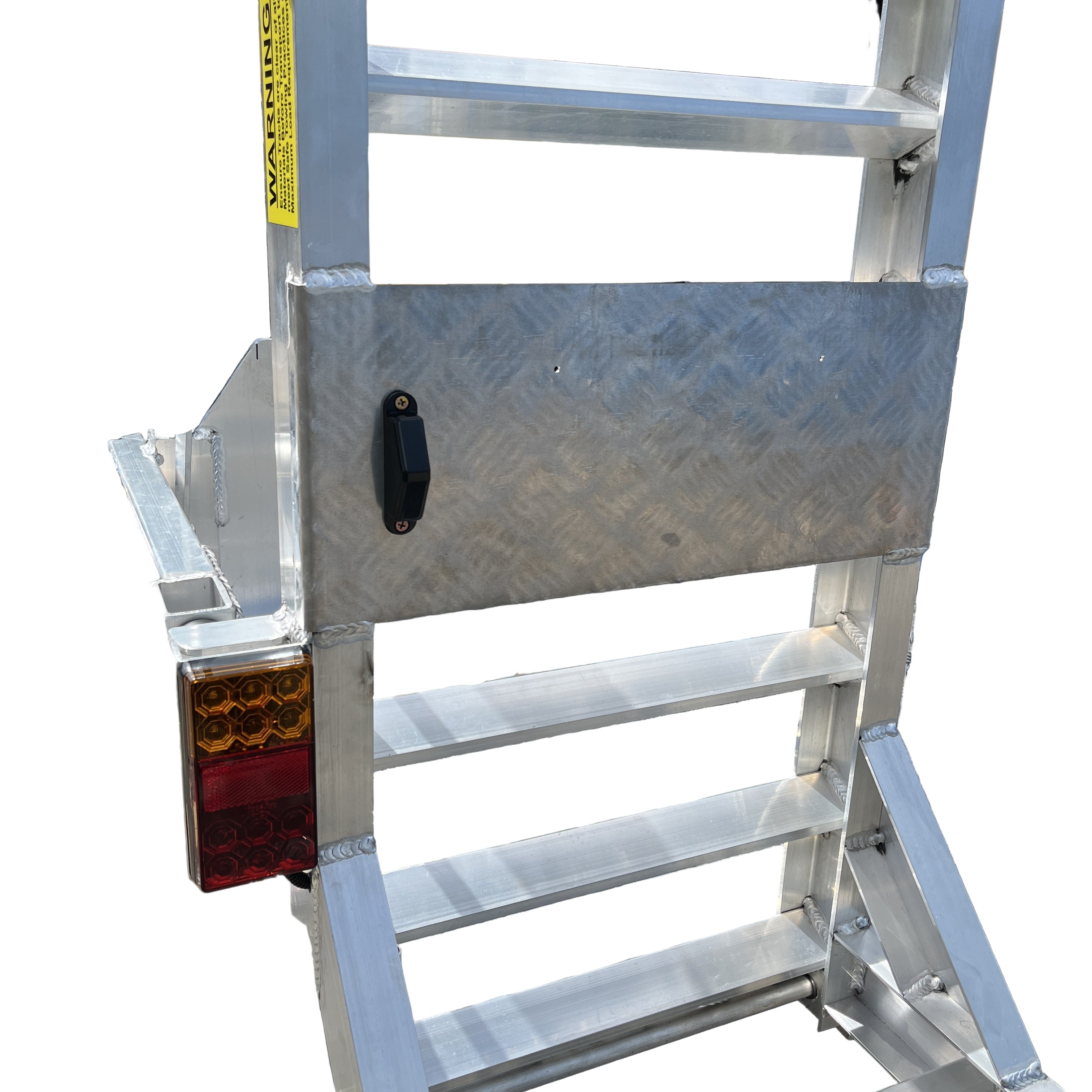 Close-up of the rear section of a Paddock Mini Loader & Excavator Alloy Equipment Trailer, showing the textured metal panel, black handle, warning label, and tail light—engineered by Paddock for heavy-duty Australian-made machinery trailers.