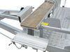 Close-up of the Paddock Mini Loader Trailer Trencher Mount, showcasing its metal frame with a wooden plank, chains, safety latches, and diamond-plate flooring; a yellow caution label is on the right. Proudly Australian made.
