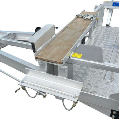 Close-up of the Paddock Mini Loader Trailer Trencher Mount, showcasing its metal frame with a wooden plank, chains, safety latches, and diamond-plate flooring; a yellow caution label is on the right. Proudly Australian made.