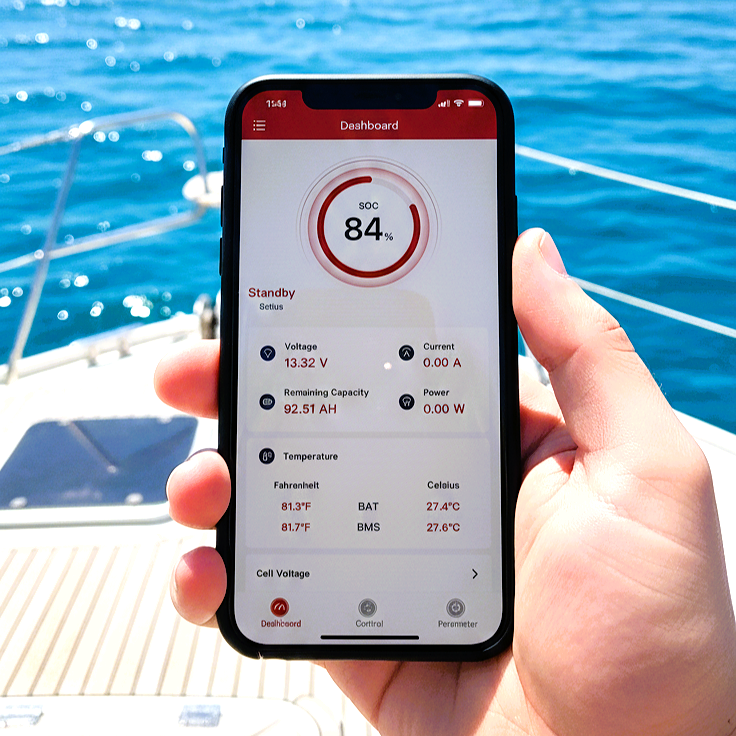 A hand holds a smartphone showing the Trolltek Bluetooth app at 84% charge, over a boat deck and blue water. The app monitors voltage, temperature, and more for the 36V Trolltek™ LiFePO4 Lithium Battery.