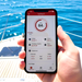 A hand holds a smartphone showing the Trolltek Bluetooth app at 84% charge, over a boat deck and blue water. The app monitors voltage, temperature, and more for the 36V Trolltek™ LiFePO4 Lithium Battery.